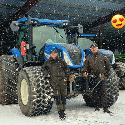 Två medarbetare som står bredvid en traktor och ler.